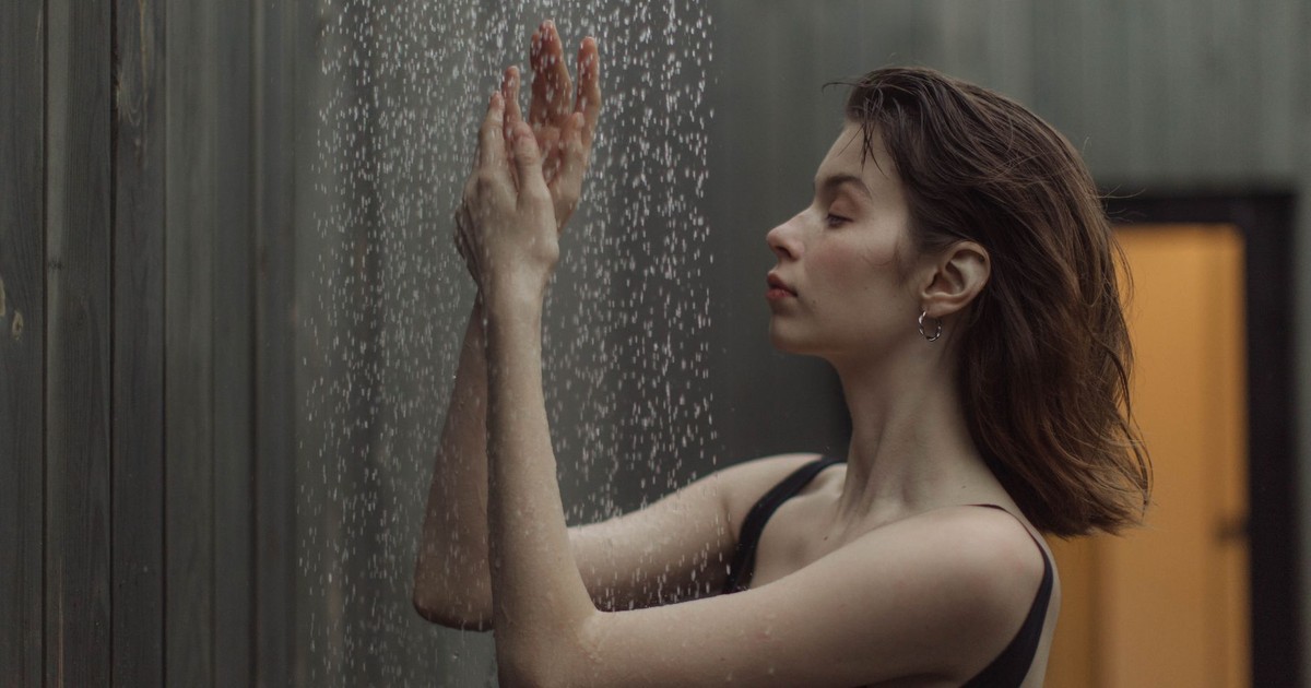 A woman savoring a tranquil moment under a gentle outdoor shower, side view.