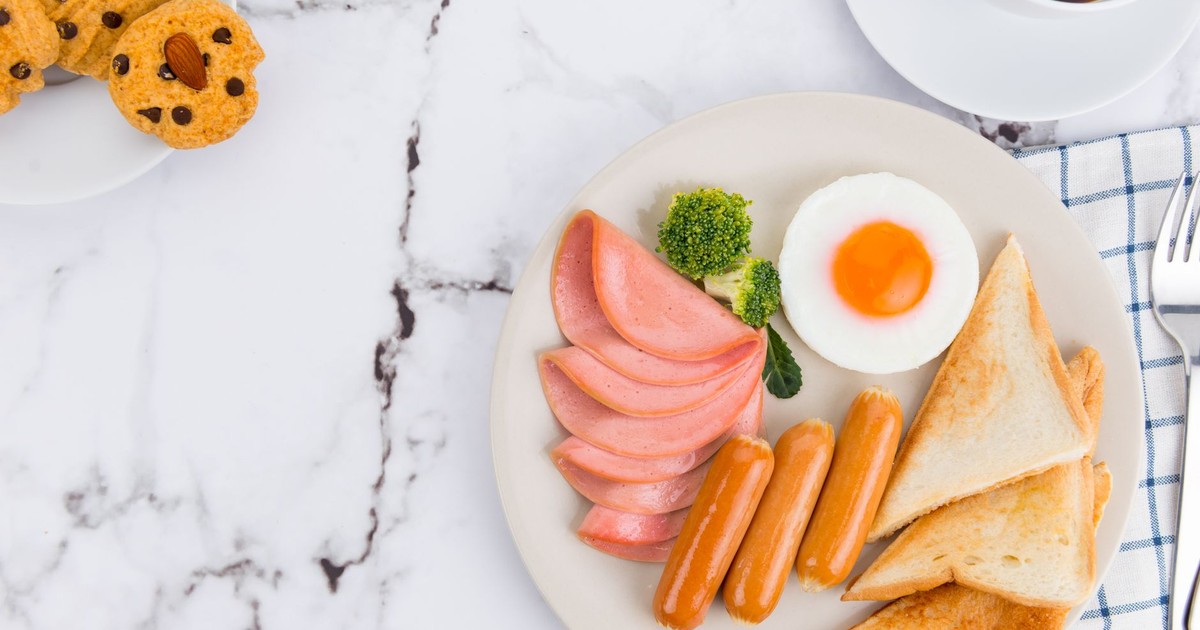 Delicious breakfast of sausages, ham, toast, egg, and coffee on a marble table.