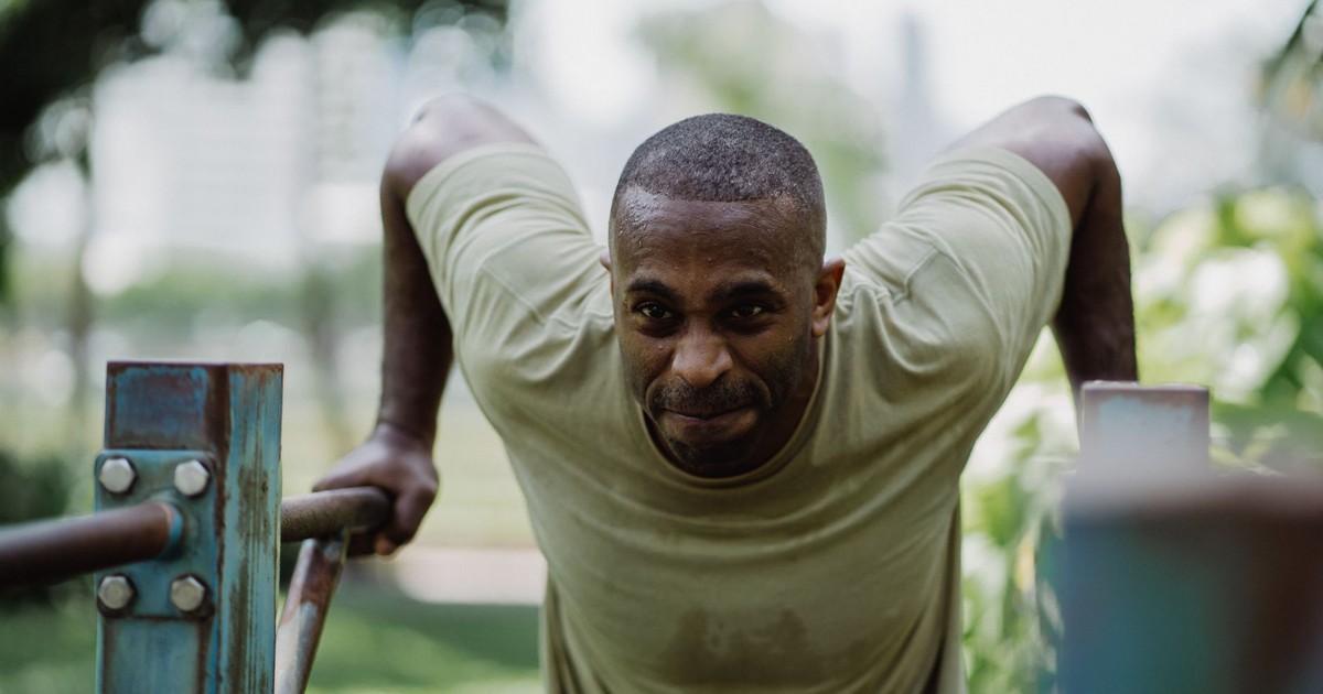 Focused athlete exercising on parallel bars outdoors, showing determination and strength.