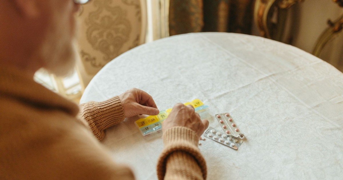 Elderly person sorting daily medication with a pill organizer on a table indoors.