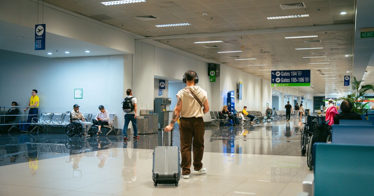 Passengers in a spacious airport terminal, some seated and others walking.