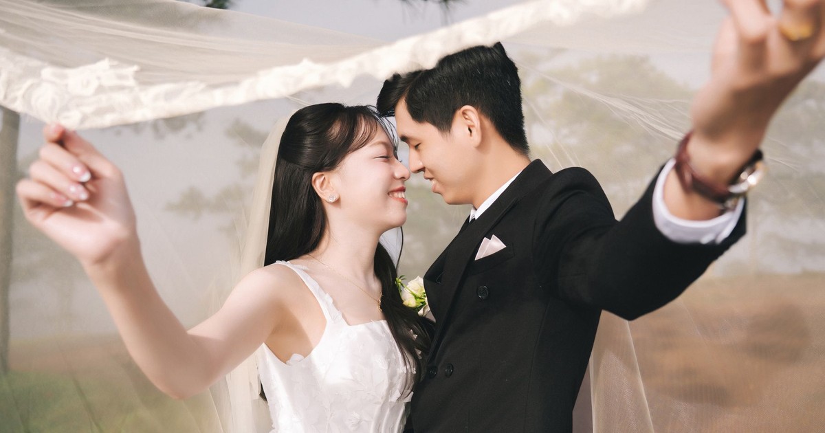 A joyful bride and groom embrace under a veil in an outdoor wedding scene.