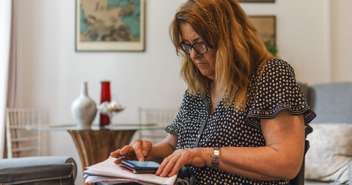 A middle-aged woman in a polka dot dress focused on her smartphone in a cozy living room setting.