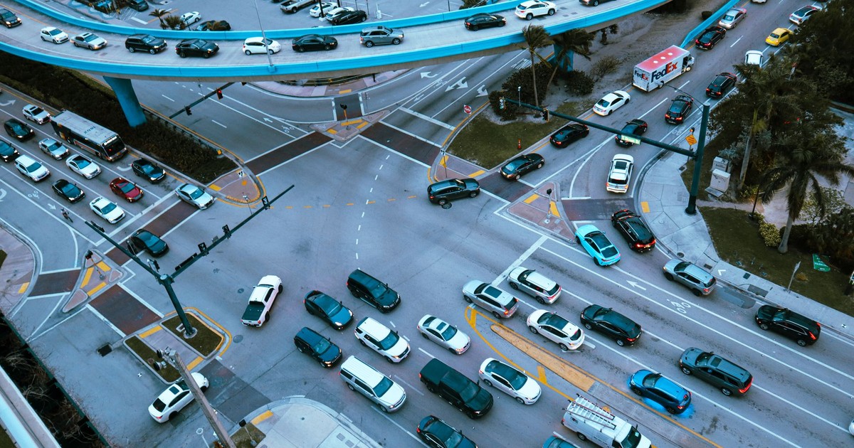 Aerial view of a busy urban intersection filled with cars and traffic under a blue overpass.
