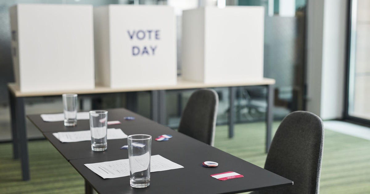 A prepared voting station with tables, chairs, and privacy booths in a conference room.