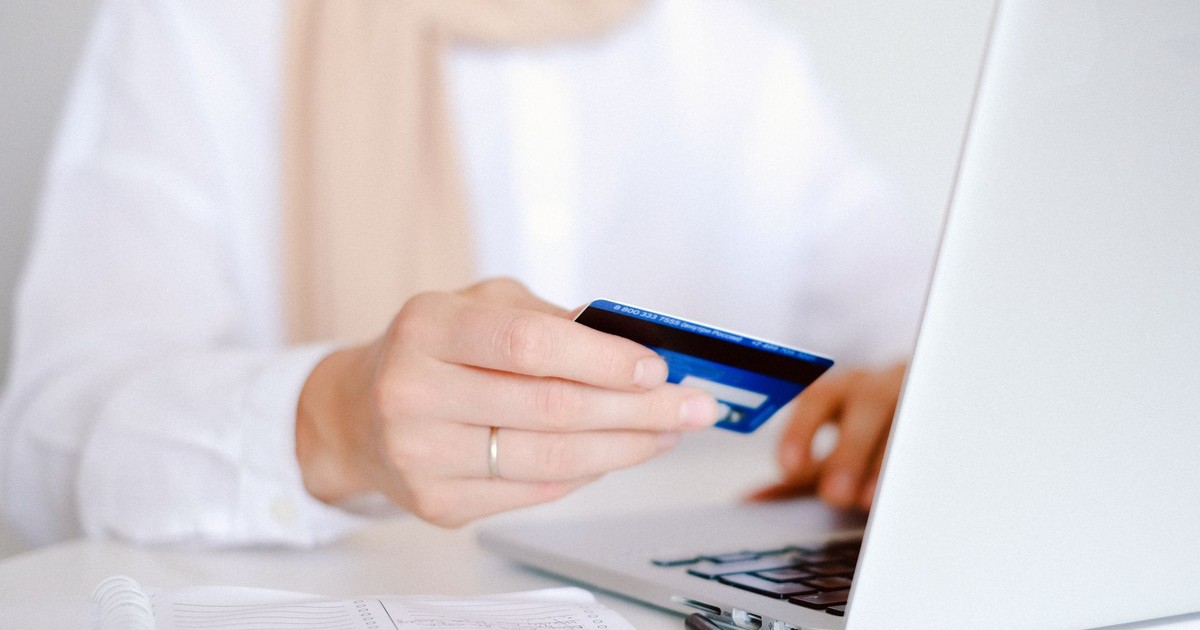 Close-up of a person holding a credit card while using a laptop for online shopping.