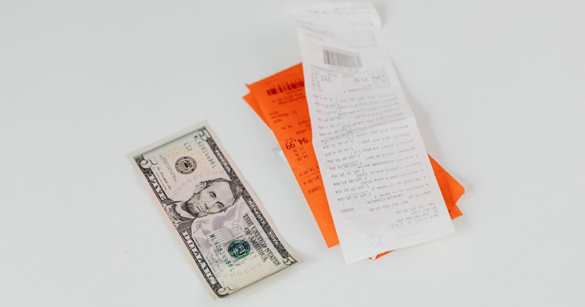 Close-up of a five-dollar bill next to shopping receipts on a white background, ideal for finance and retail themes.