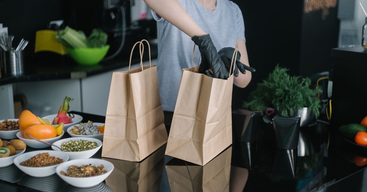 A person in a kitchen packing food ingredients into paper bags for takeout orders.