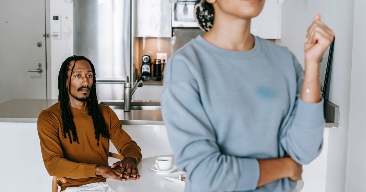 Young black man sitting at table while having conflict with standing near table woman in light kitchen
