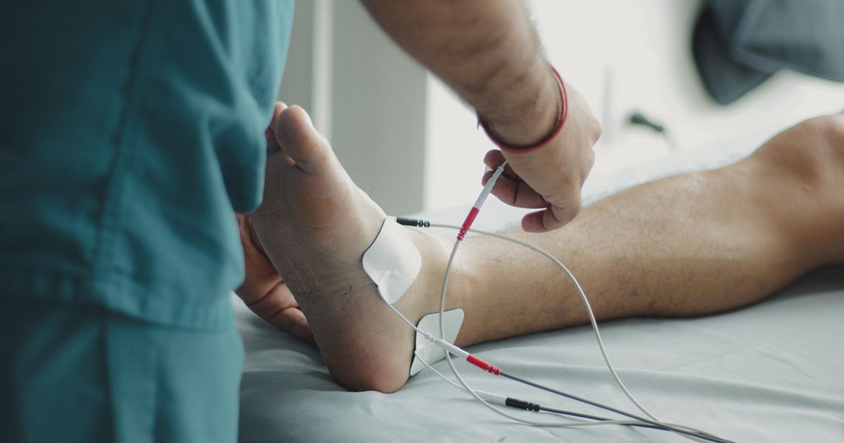 Close-up of a healthcare worker examining a patient's foot with medical equipment in a hospital setting.