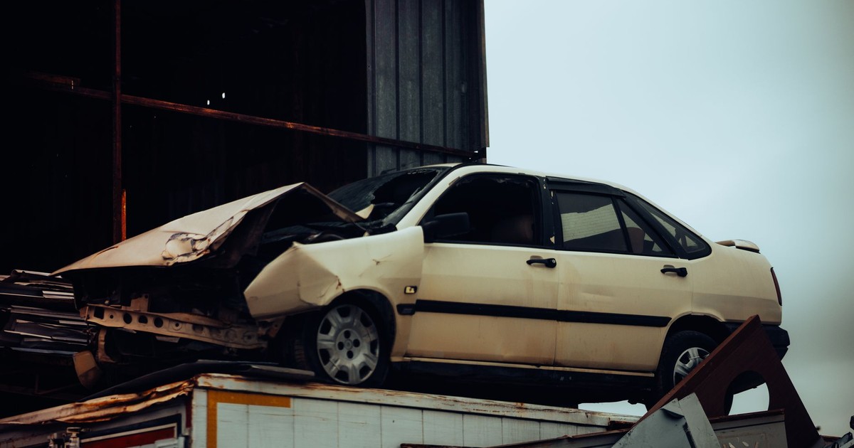 A damaged car sits atop a metal scrap heap, showing a scene of automotive decay.