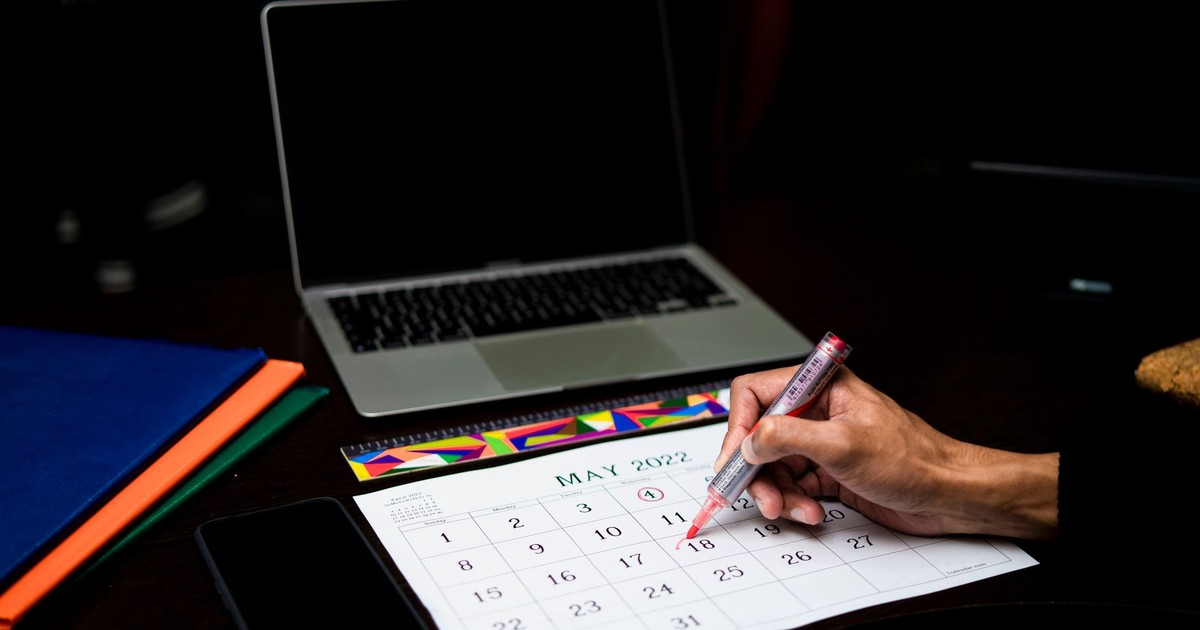 A person plans on a calendar at a desk with a laptop and phone, May 2022.