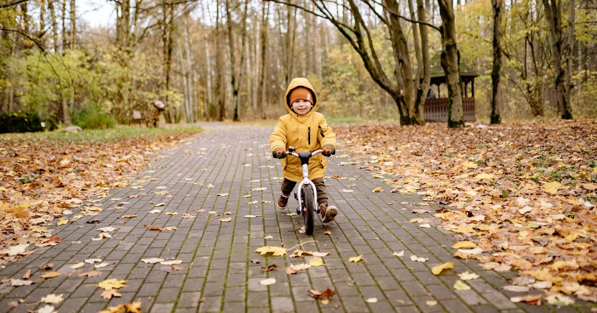 Smiling child riding a bike on a leaf-covered path in an autumn park, experiencing joy and fun.