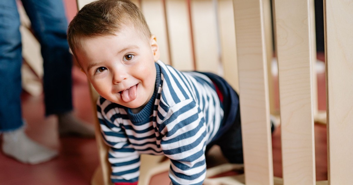 Cute child in striped shirt crawling and playing indoors with a playful expression.