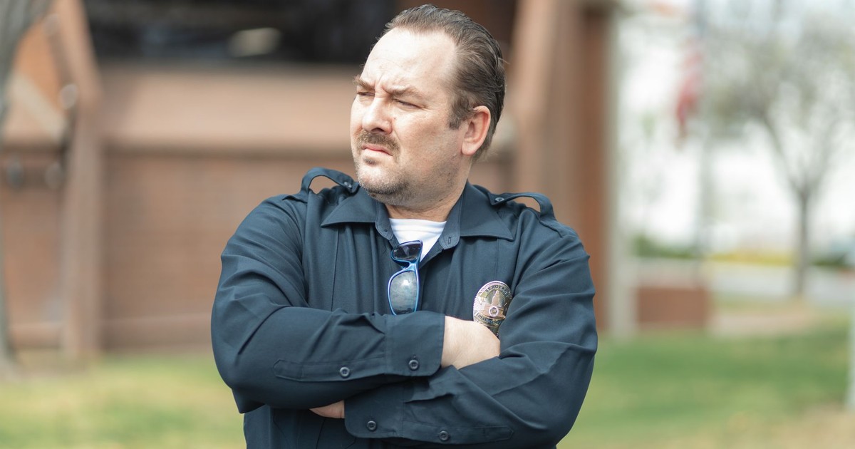 Law enforcement officer standing confidently with arms crossed outdoors in uniform.