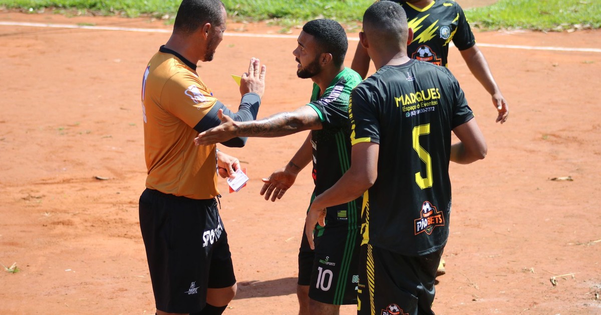 A heated moment on the field as a referee shows a card to a player during a sunny soccer match.