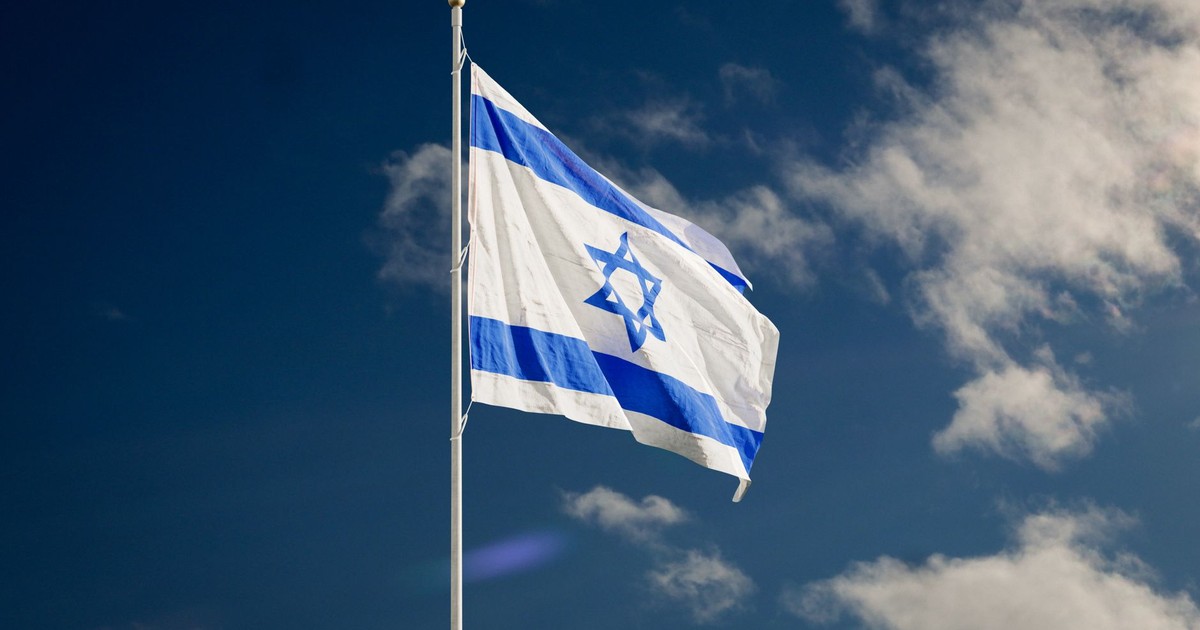 The Israeli national flag waving against a clear blue sky with clouds.