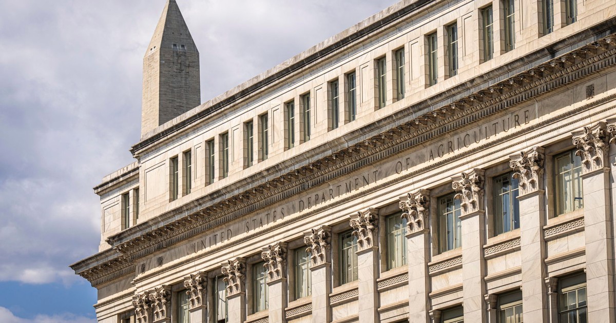 US Department of Agriculture building with Washington Monument behind, blue sky with clouds.
