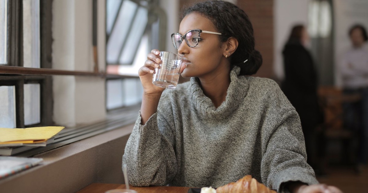 African American woman sipping water with a croissant at a cafe. Cozy indoor setting.