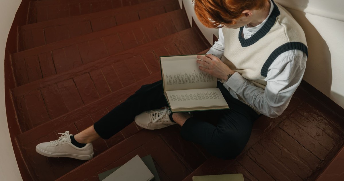 A young man reading a book while sitting on a rustic wooden staircase, exuding concentration and tranquility.