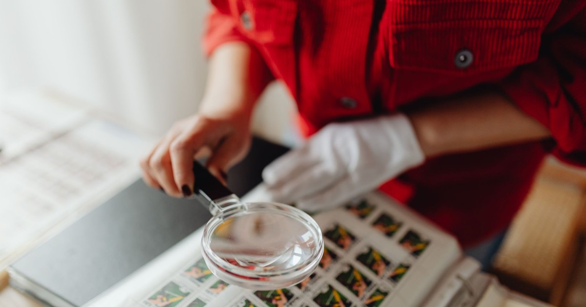 A person closely examines postage stamps with a magnifying glass, revealing intricate details.