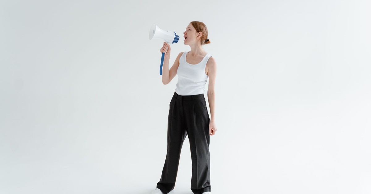 Woman in casual attire speaking through a megaphone in a bright studio setting.