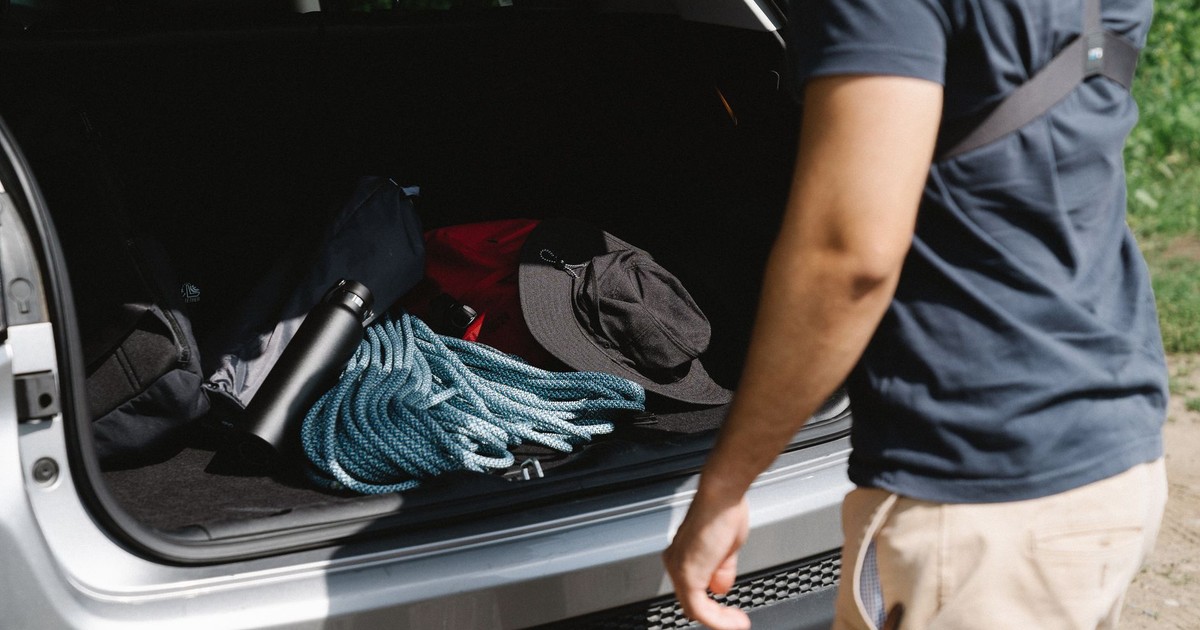Man organizing camping gear in car trunk, ready for adventure.