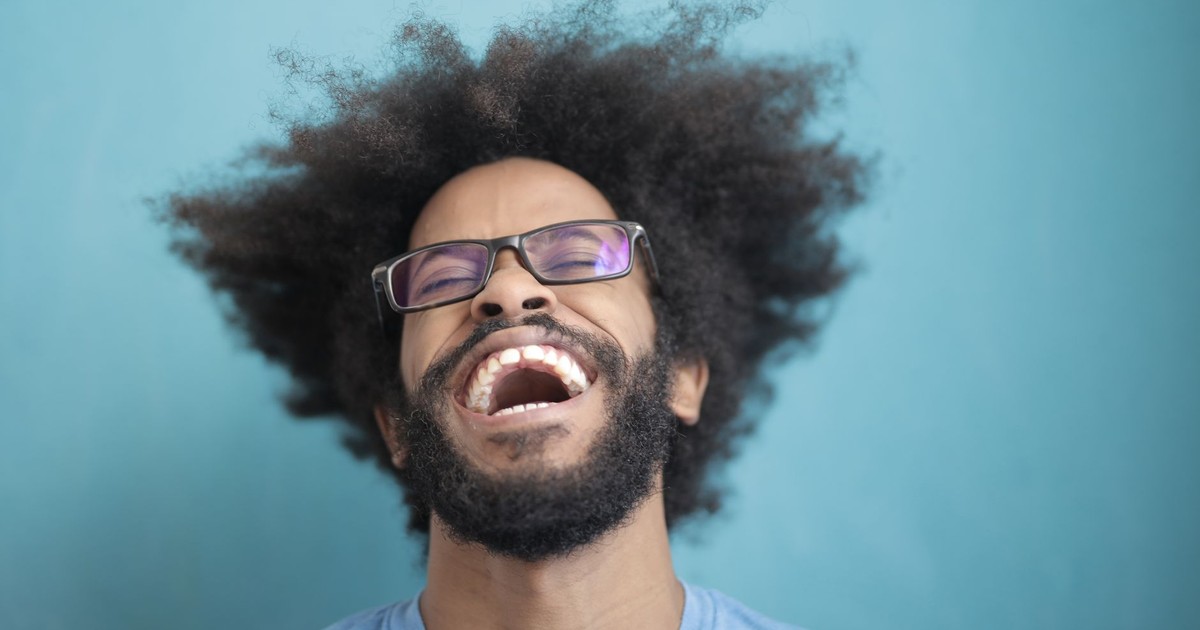 Portrait of a joyful man laughing with an afro hairstyle against a blue background.