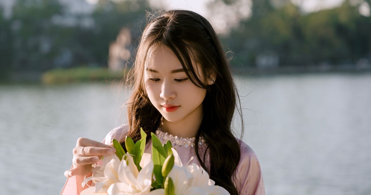 A young woman in traditional dress holds a bouquet of white lilies by a tranquil lake.