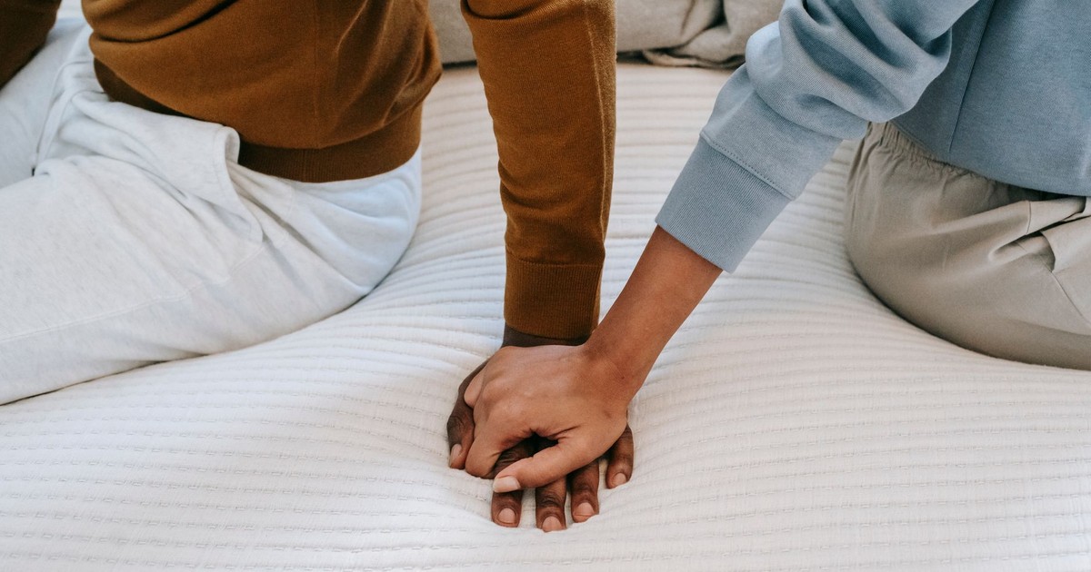Crop faceless African American couple sitting on bed back to back and holding hands