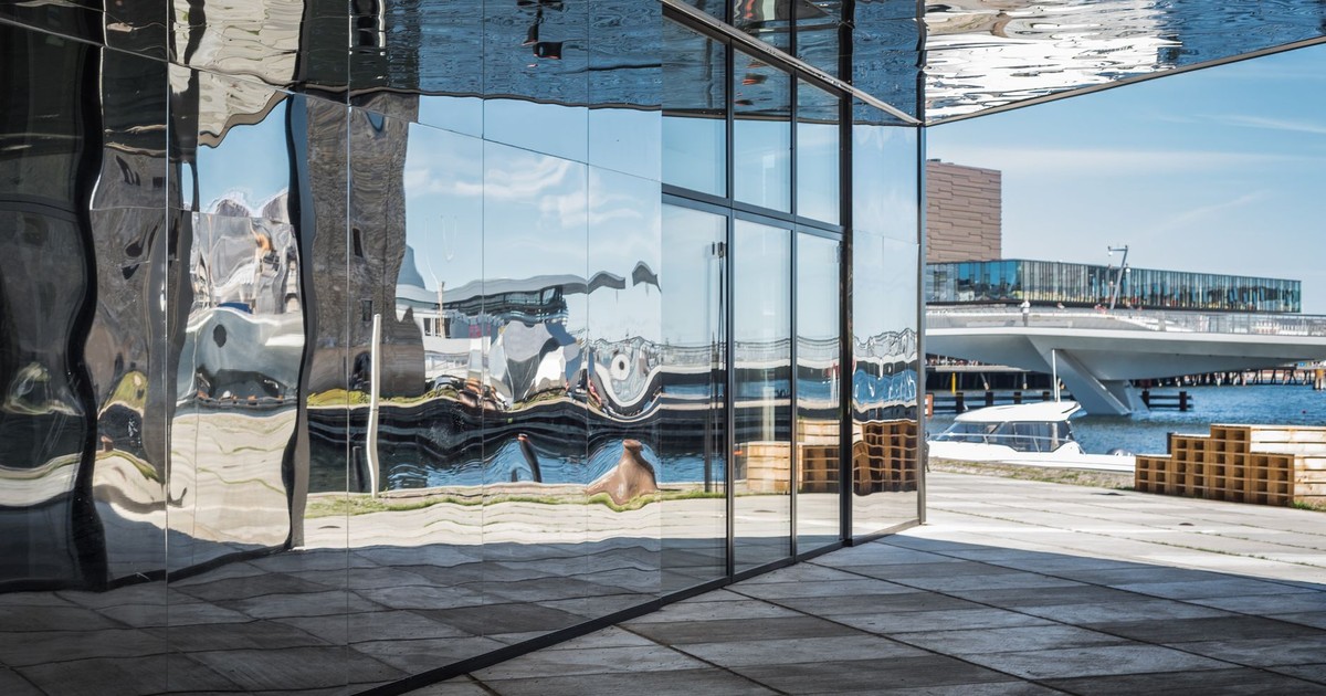Modern architecture reflecting urban waterfront scenery in Copenhagen, featuring distorted reflections in glass surfaces.