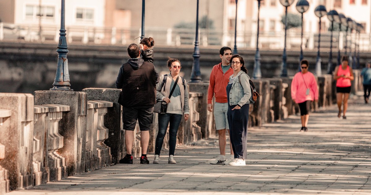 Group of people enjoying a sunny walk on a promenade in Burgo, Spain.