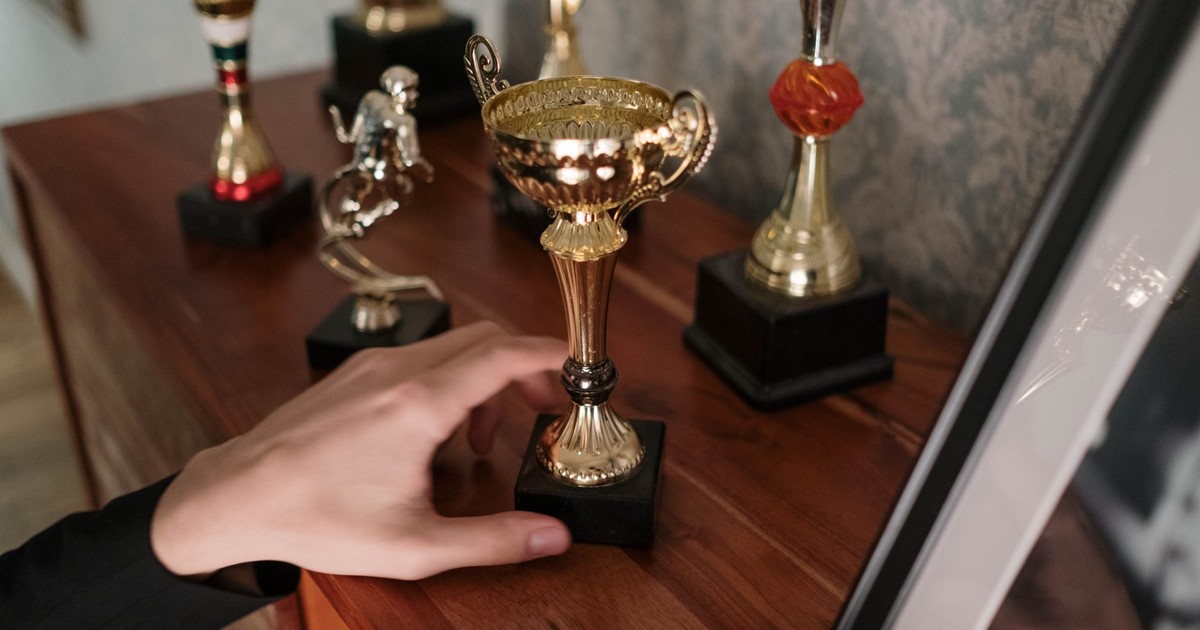 A close-up of a hand reaching for a shiny trophy on a wooden shelf, symbolizing success.