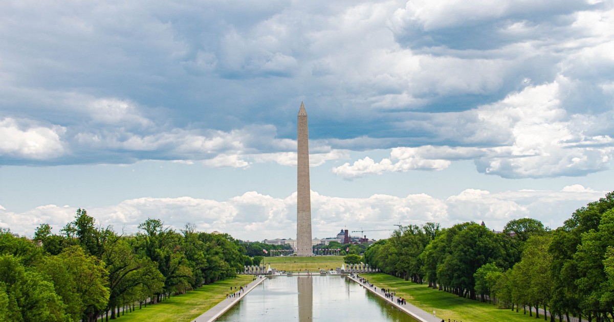 A scenic view of the Washington Monument in Washington, D.C., with reflections in the reflecting pool and a cloudy sky overhead.