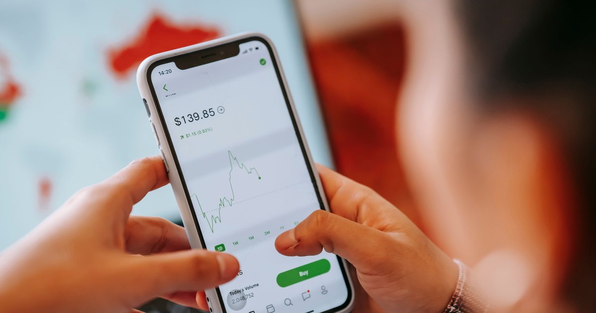 Crop anonymous trader using app on cellphone with graph and dollar price on screen in house