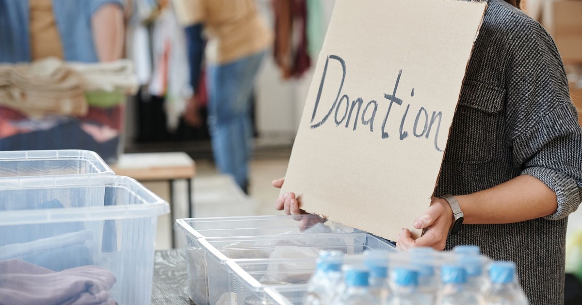 A volunteer holds a cardboard donation sign at a charity event with donation boxes ready for collection.