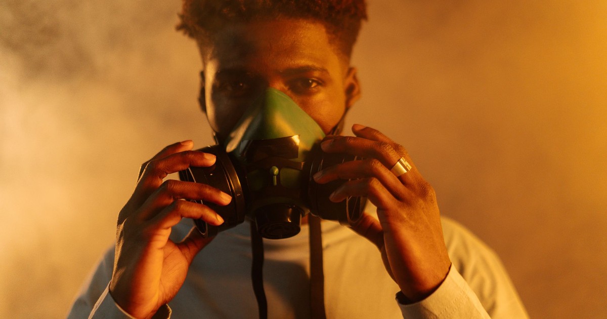 An adult man wearing a gas mask amidst smoke, emphasizing air pollution and protection themes.