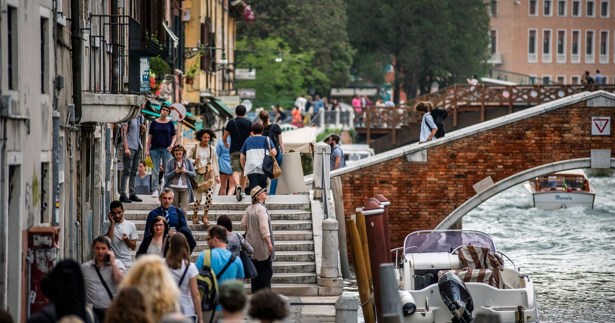 A crowded scene in Venice along a canal with tourists, boats, and historic architecture.