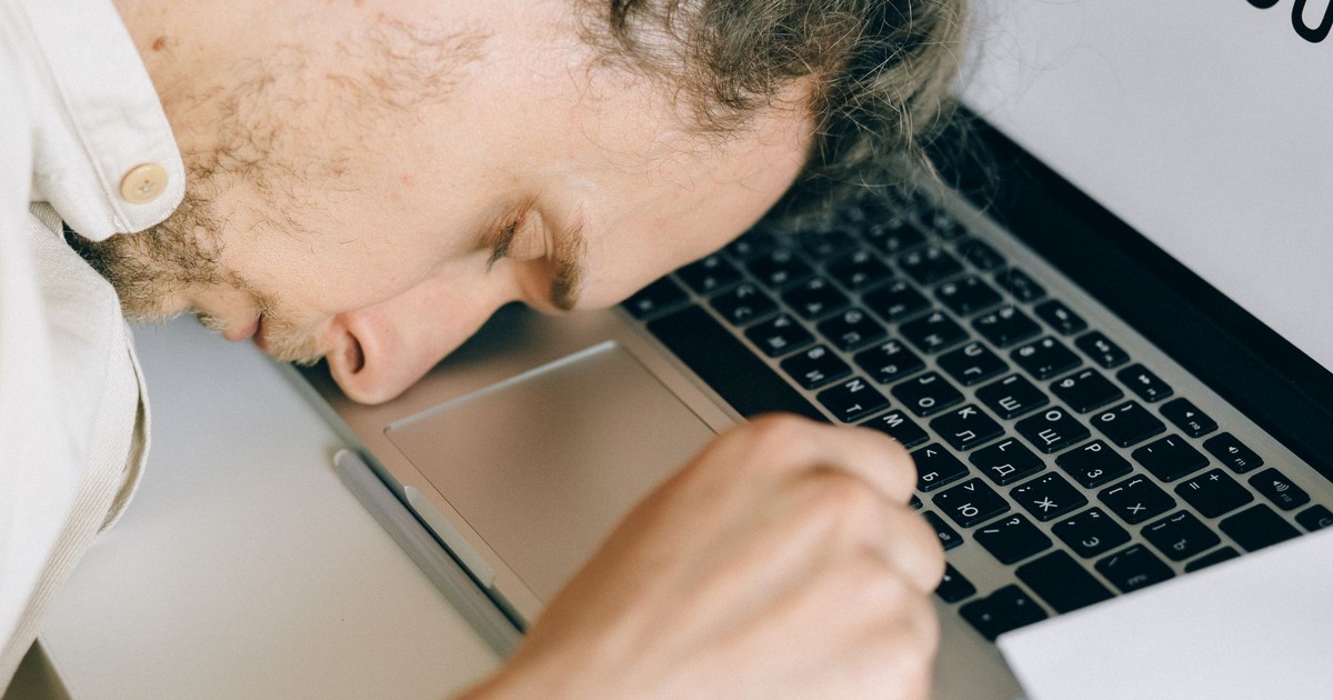 Exhausted employee resting head on laptop keyboard due to burnout and stress.