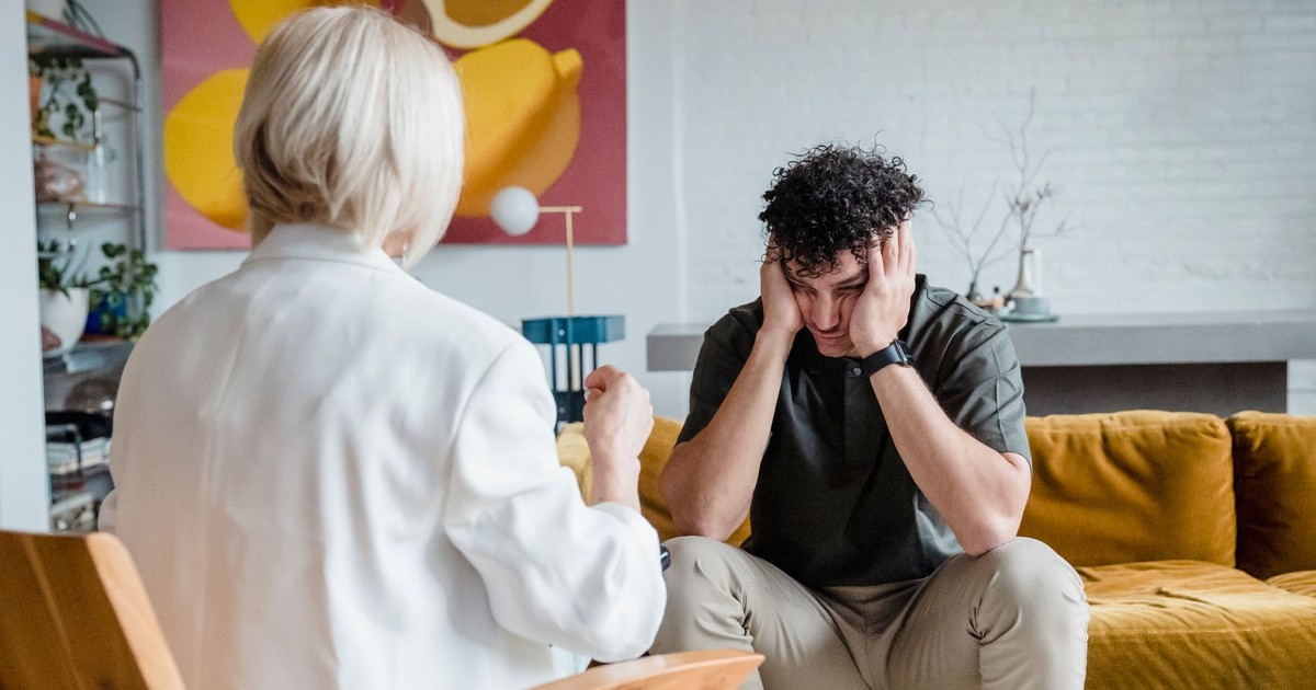 A therapist consults a distressed man in a cozy setting.