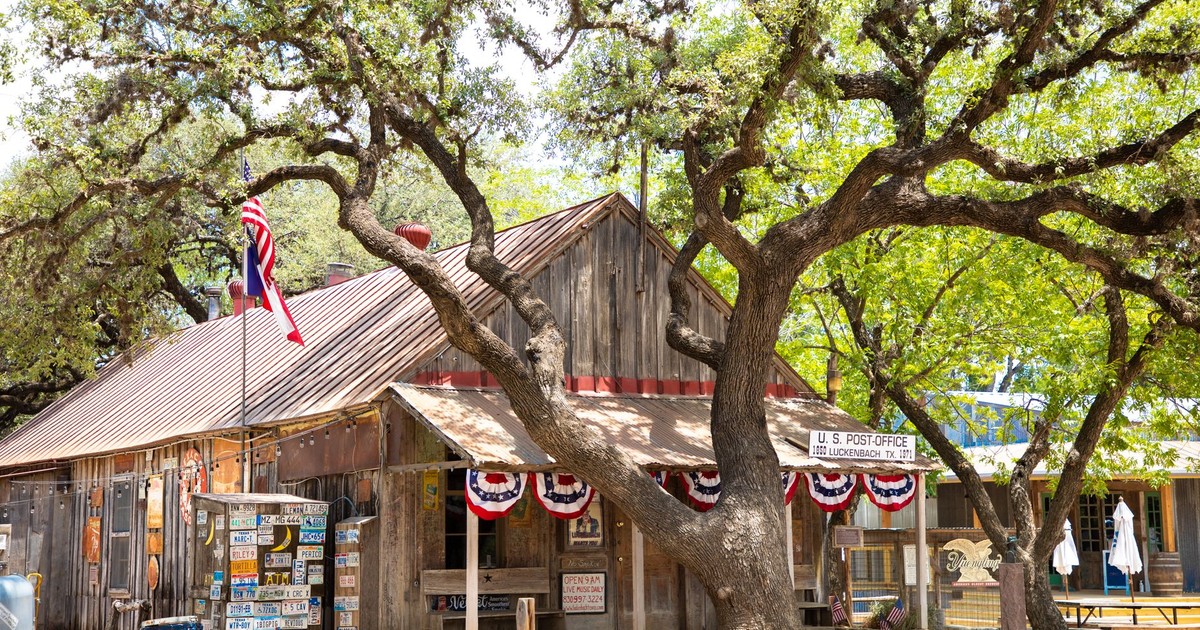 Rustic wooden post office in Luckenbach, Texas, with American flag and oak tree.