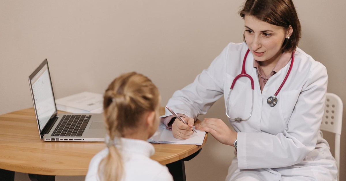 A female doctor listens attentively to a young girl during a medical consultation in an office setting.